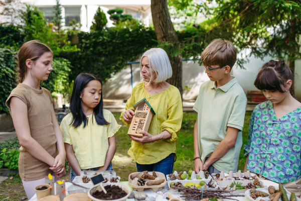 Insect hotel as educational tool for children in outdoor sustainable educational class. Young students learning about insect and biodiversity, holding wooden bug house.