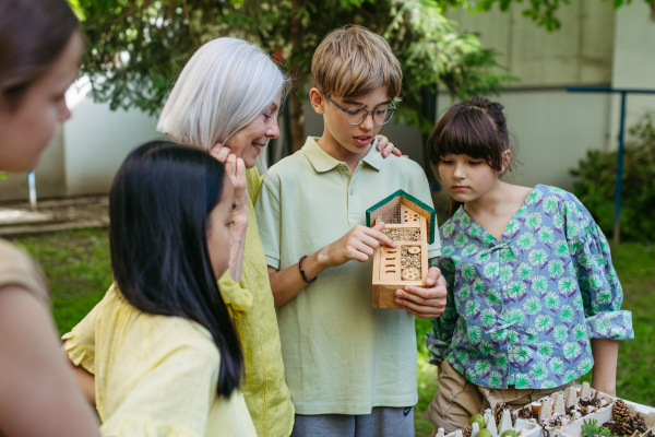 Insect hotel as educational tool for children in outdoor sustainable educational class. Young students learning about insect and biodiversity, holding wooden bug house.