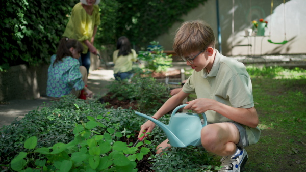 Students and female teacher at outdoor sustainable education class. Kids taking care of plants in school garden. Concept of experiential learning, ecoliteracy.