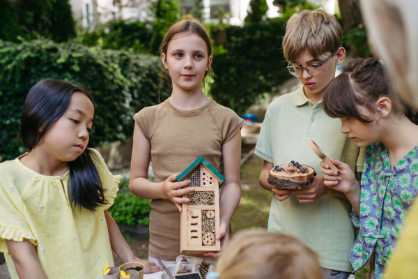 Insect hotel as educational tool for children in outdoor sustainable educational class. Young students learning about insect and biodiversity, holding wooden bug house.