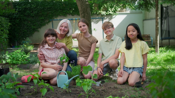 Students and female teacher at outdoor sustainable education class. Kids taking care of plants in school garden. Concept of experiential learning, ecoliteracy.