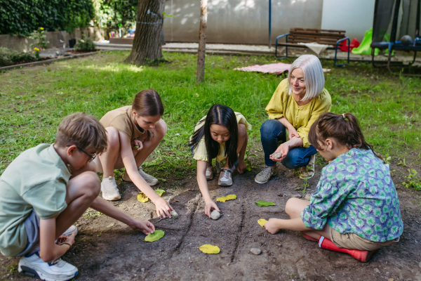 Students playing tic-tac-toe with stones and leaves, grid in soil, having fun. Outdoor sustainable education class.