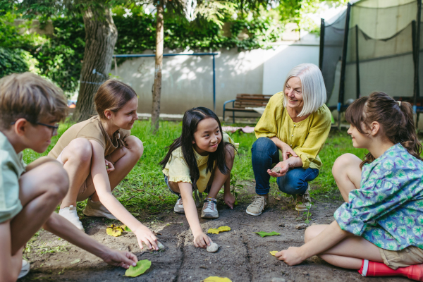 Students playing tic-tac-toe with stones and leaves, grid in soil, having fun. Outdoor sustainable education class.