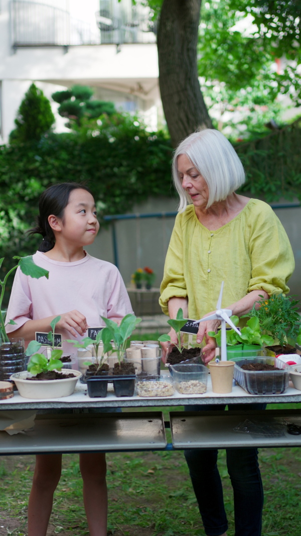 Girl student growing vegetable and herb seedlings, teacher helping her. Outdoor sustainable education class in school garden Concept of experiential learning, ecoliteracy.