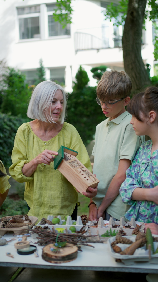 Insect hotel as educational tool for children in outdoor sustainable educational class. Young students learning about insect and biodiversity, holding wooden bug house.