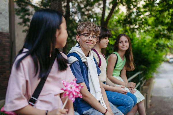 Four friends classmates with backpack sitting outdoors, waiting for bus.