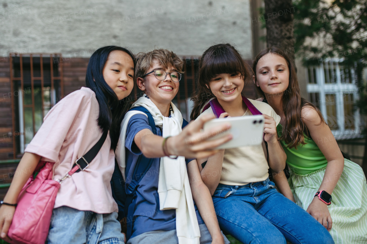 Four friends taking selfie with smartphone outdoor.