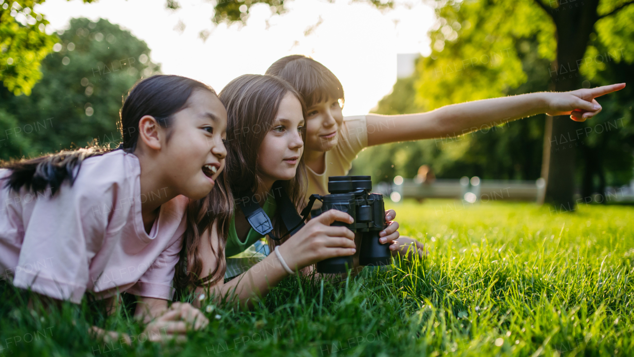 Young girl students learning about nature and wildlife in urban environment, using binoculars and observing animals, birds in public park.