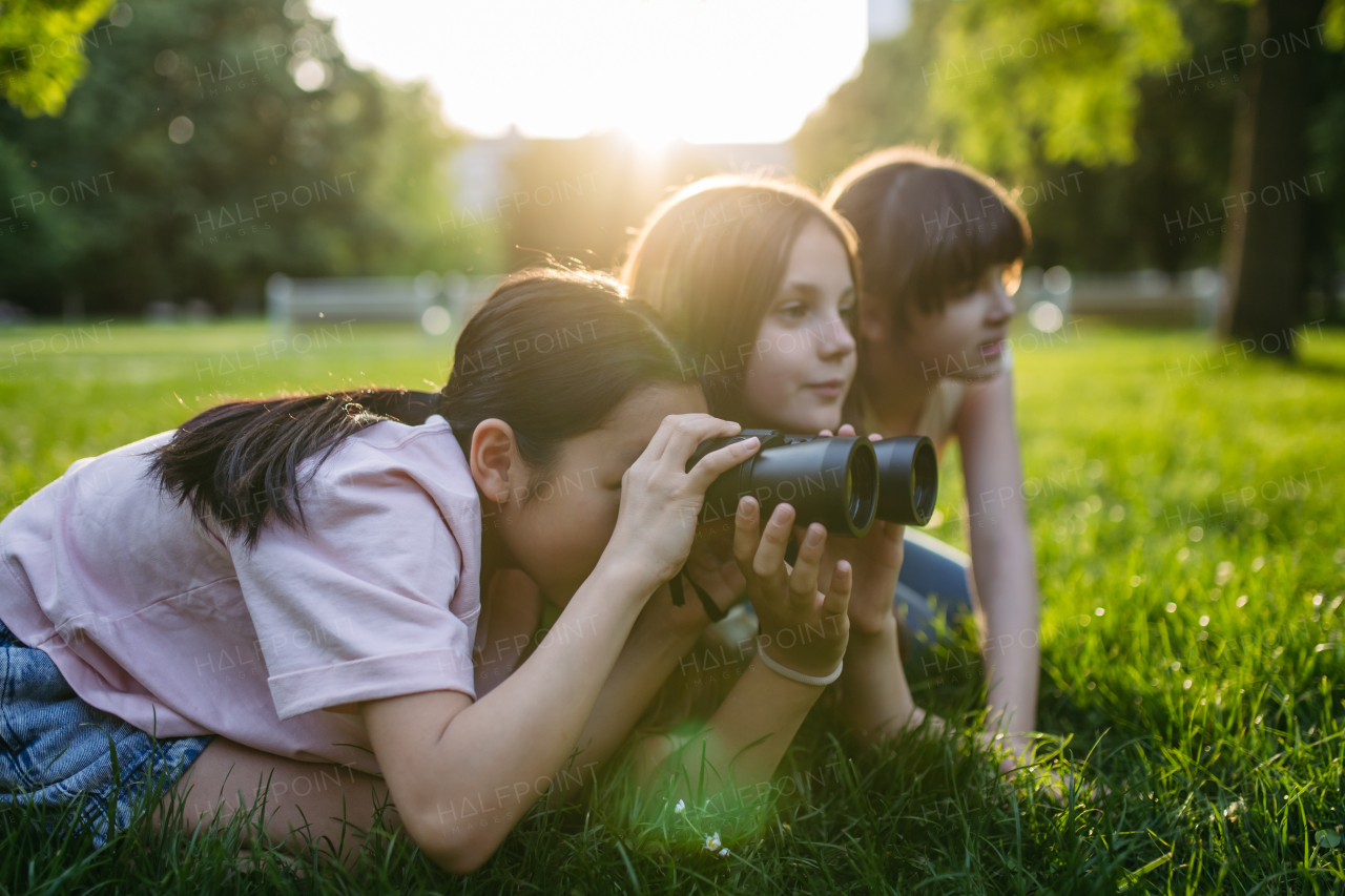 Young girl students learning about nature and wildlife in urban environment, using binoculars and observing animals, birds in public park.