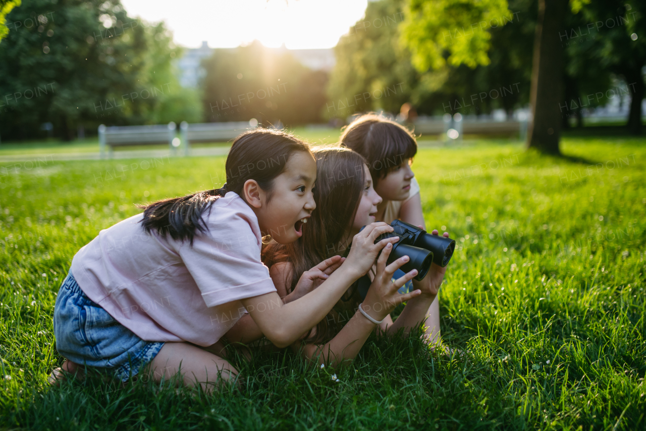 Young girl students learning about nature and wildlife in urban environment, using binoculars and observing animals, birds in public park.