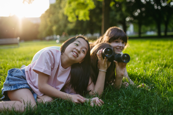 Young girl students learning about nature and wildlife in urban environment, using binoculars and observing animals, birds in public park.