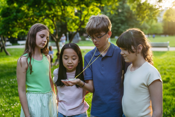 Group of children in outdoor sustainable educational class using compass learning orienteering in public park.