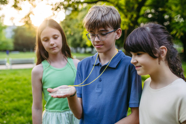 Group of children in outdoor sustainable educational class using compass learning orienteering in public park.