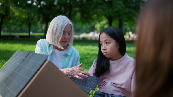 Children learning about renewable solar energy during sustainable education class outdoors, using cardboard model of house wit solar panel on roof.