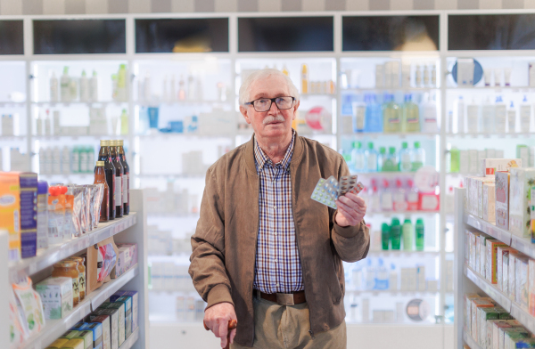 Portrait of senior man holding medicine,standying in pharmacy store.