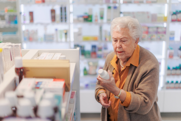 Senior woman reading text on the medication box, standing in pharmacy store.