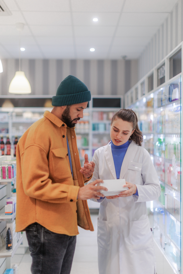 Young pharmacist helping customer to choos a medication.