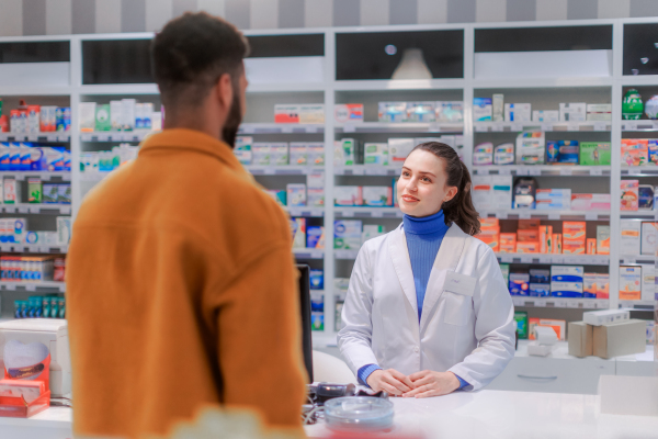 Young pharmacist selling medications to a customer.