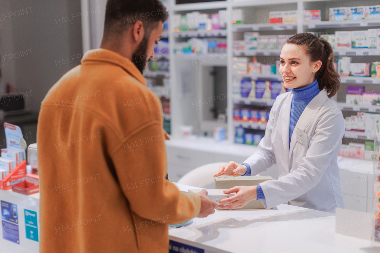 Young pharmacist selling medications to a customer.