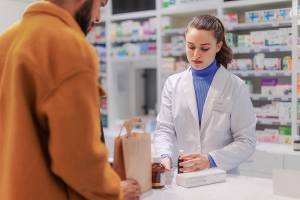 Young pharmacist selling medications to a customer.