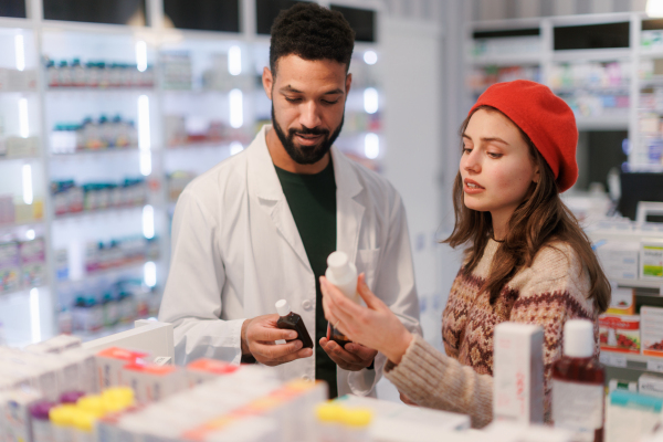 Young pharmacist helping customer to choos a medication.