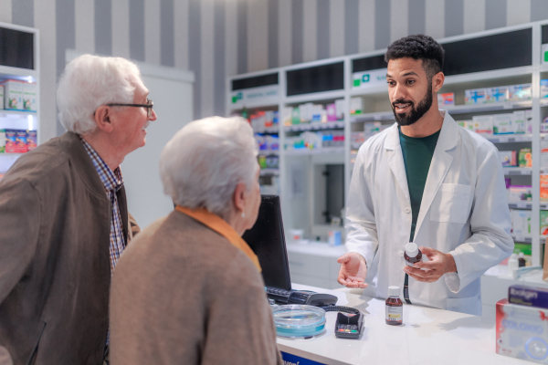 Young pharmacist selling medications to senior couple in a pharmacy store.