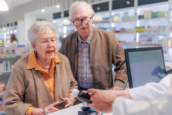 Young pharmacist selling medications to senior couple in a pharmacy store.