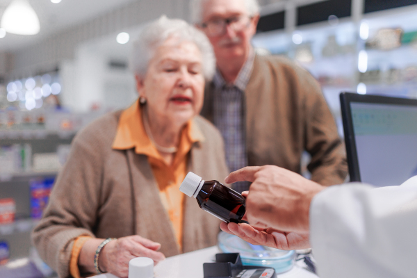 Young pharmacist selling medications to senior couple in a pharmacy store.