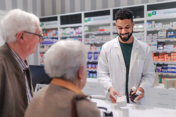 Young pharmacist selling medications to senior couple in a pharmacy store.