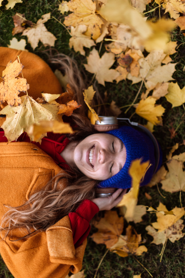 Young woman listening music outdoor,lying in the autumn nature.