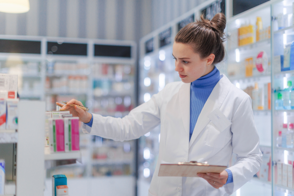 Young pharmacist checking medicine stock in a pharmacy.