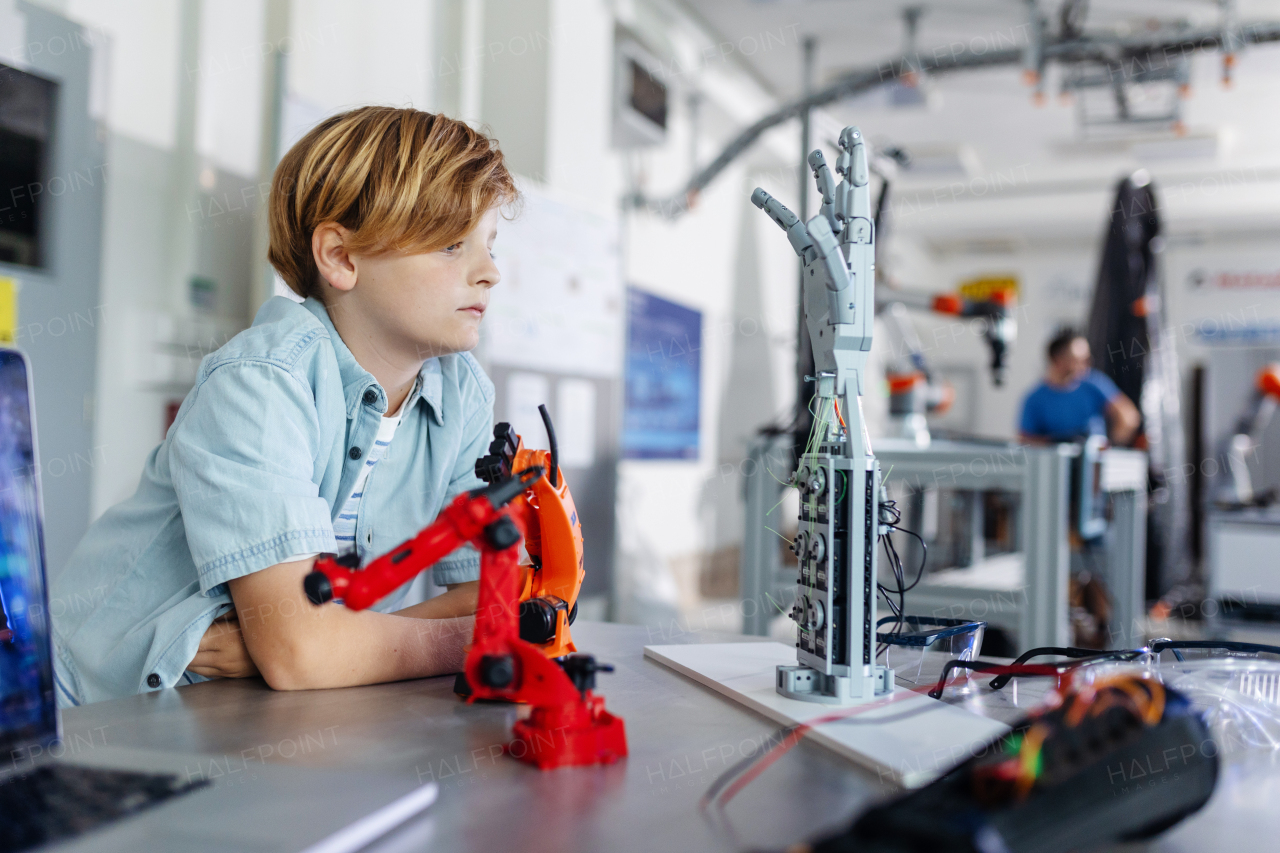 Portrait of curious schoolboy looking robotic arm and hand, after-school robotics club. Children learning robotics in Elementary school. Science for kids.