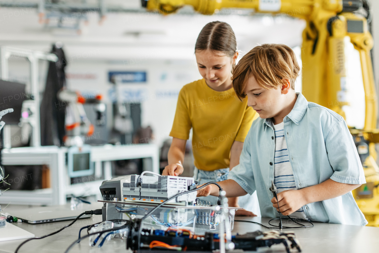 Two classmates working togeter on circuit board, building robot in an after-school robotics club. Children learning robotics in Elementary school.