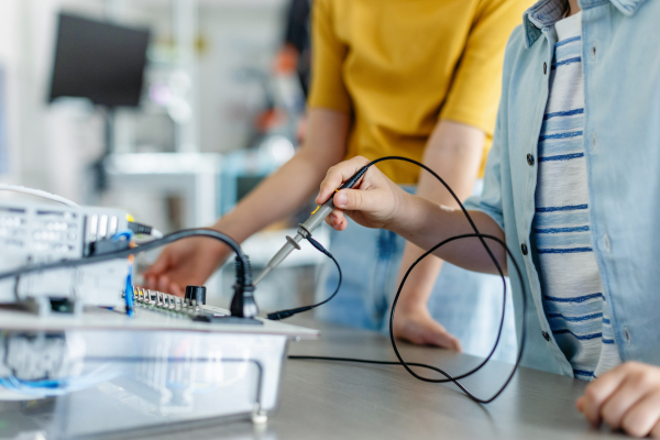 Two classmates working together on circuit board, building robot in an after-school robotics club. Children learning robotics in Elementary school.