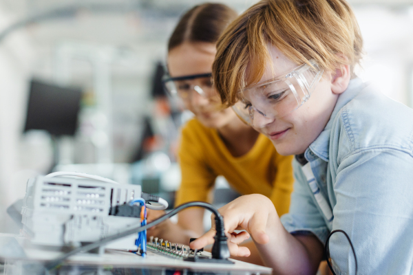 Two classmates working together on circuit board, building robot in an after-school robotics club. Children learning robotics in Elementary school.