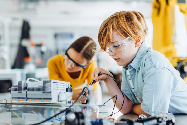 Two classmates working together on circuit board, building robot in an after-school robotics club. Children learning robotics in Elementary school.