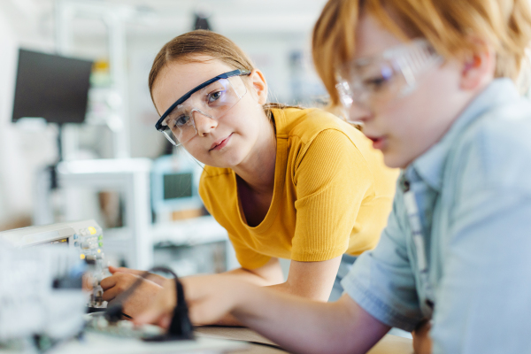 Two classmates working together on circuit board, building robot in an after-school robotics club. Children learning robotics in Elementary school.