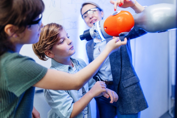 Field trip to real robotics laboratory, encouraging children in career in robotics. Real scientist talking with young students, showing them a robotic arm.