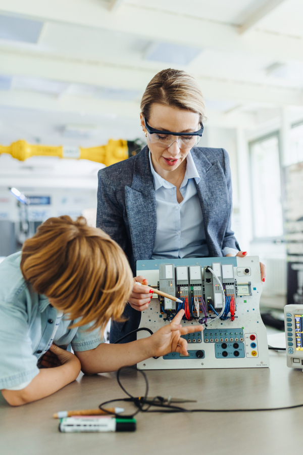 Female teacher explaining circuit board to schoolboy in after-school robotics club. Children learning robotics in Elementary school. Science for kids. STEM.