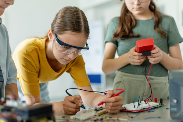 School girls working on circuit board of small robot, building robotic car in after-school robotics club. Children learning robotics in Elementary school. Girls in science, STEM.