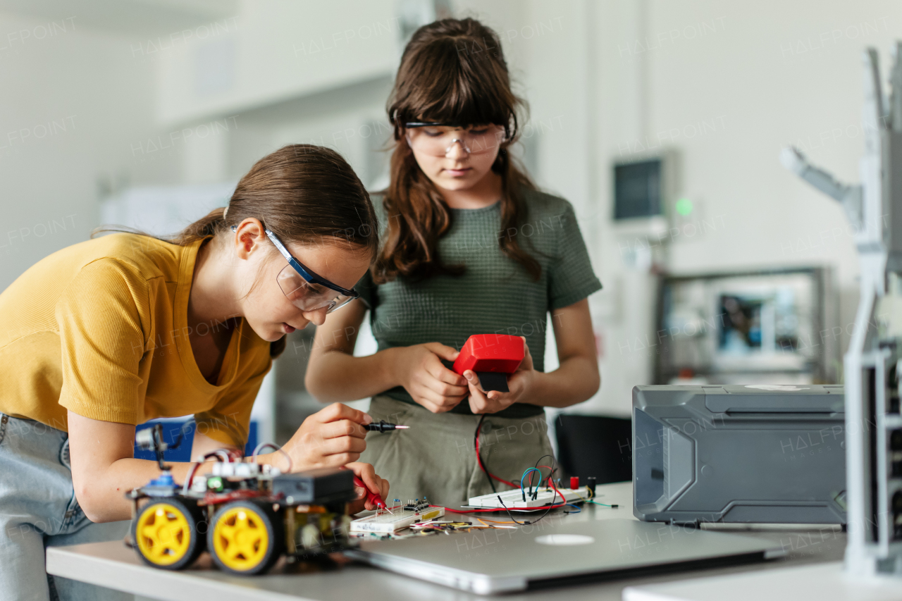 Two girl classmates working togeter on circuit board, building robotic car in an after-school robotics club. Children learning robotics in Elementary school.