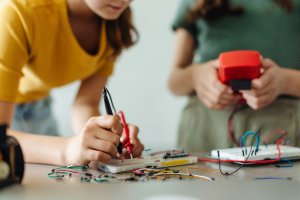 School girls working on circuit board of small robot, building robotic car in after-school robotics club. Children learning robotics in Elementary school. Girls in science, STEM.