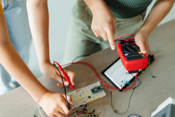 Classmates working togeter on circuit board, building robot in an after-school robotics club. Children learning robotics in Elementary school.