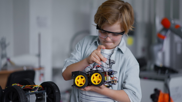 Portrait of focused schoolboy building robotic car in after-school robotics club. Children learning robotics in Elementary school. Science for kids.