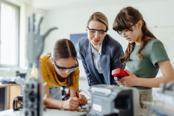 Female teacher helping to girls working on small robot, working together on circuit board in after-school robotics club. Children learning robotics in Elementary school. Girls in science, STEM.