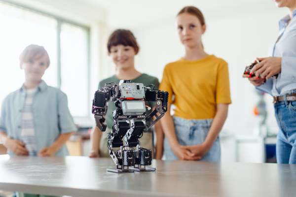 Children learning robotics in Elementary school, looking at small robot on desk. Young students building robot in after school robotics club. Field trip to real robotics laboratory.