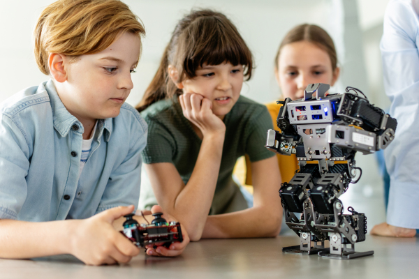 Children looking at small robot, learning robotics in elementary school. Young students building robot in after school robotics club.