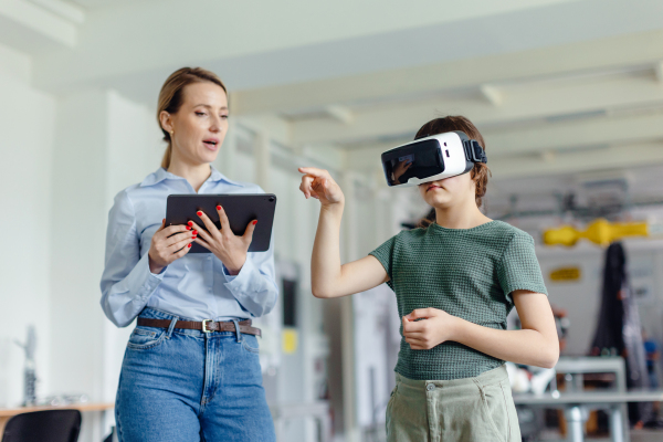 Schoolgirl learning with VR headset on head. Teacher using modern technology, virtual reality in classroom.