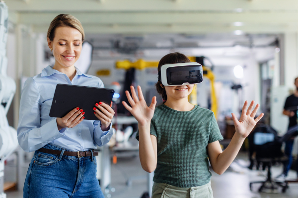 Schoolgirl learning with VR headset on head. Teacher using modern technology, virtual reality in classroom.