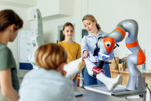 Field trip to real robotics laboratory, encouraging children in career in robotics. Real scientist talking with young students, showing them a robotic arm.